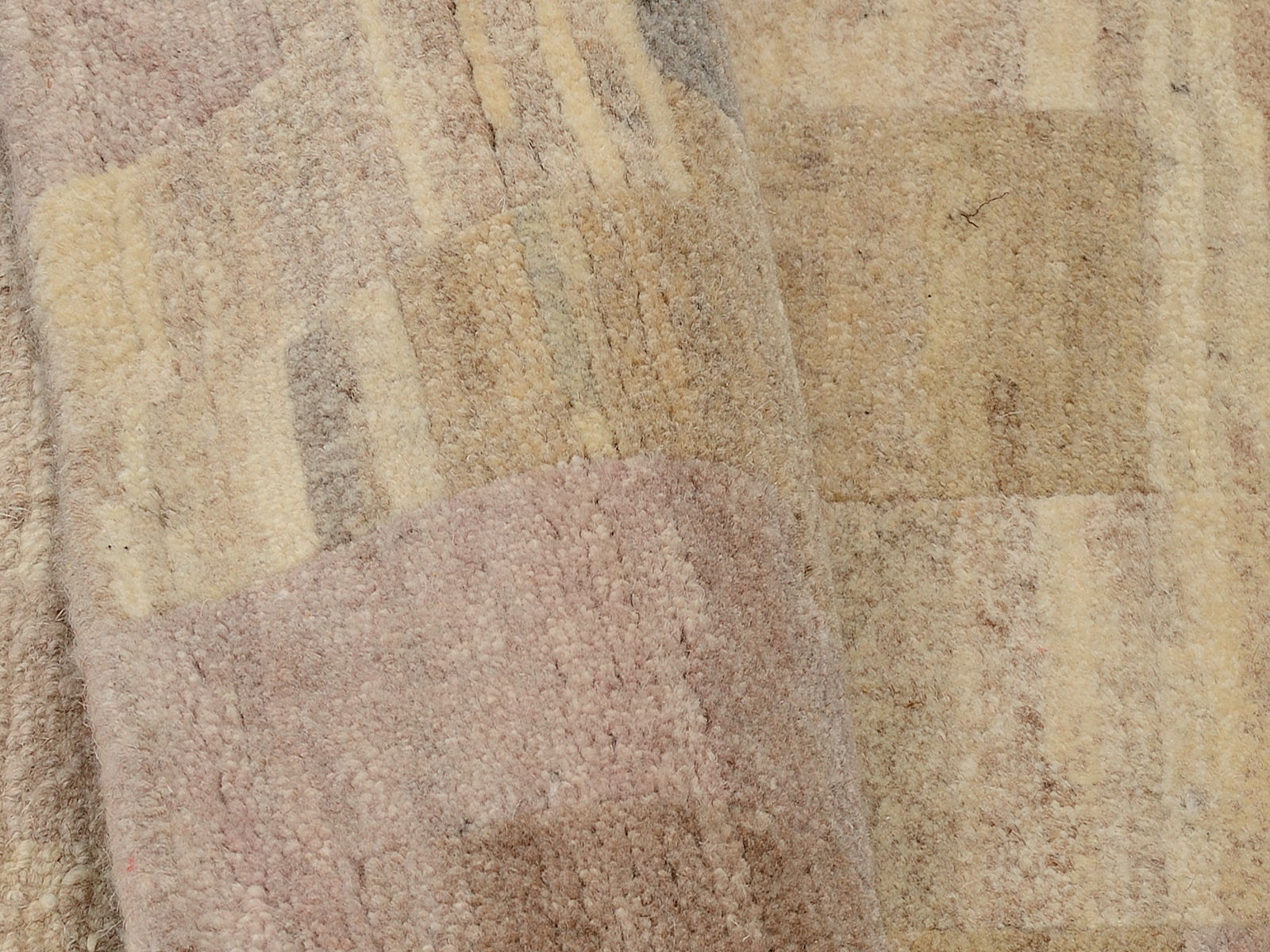 Nahaufnahme eines Wollteppichs mit geometrischem Muster in sanften Beige- und Rosatönen, aus seitlicher Perspektive fotografiert.