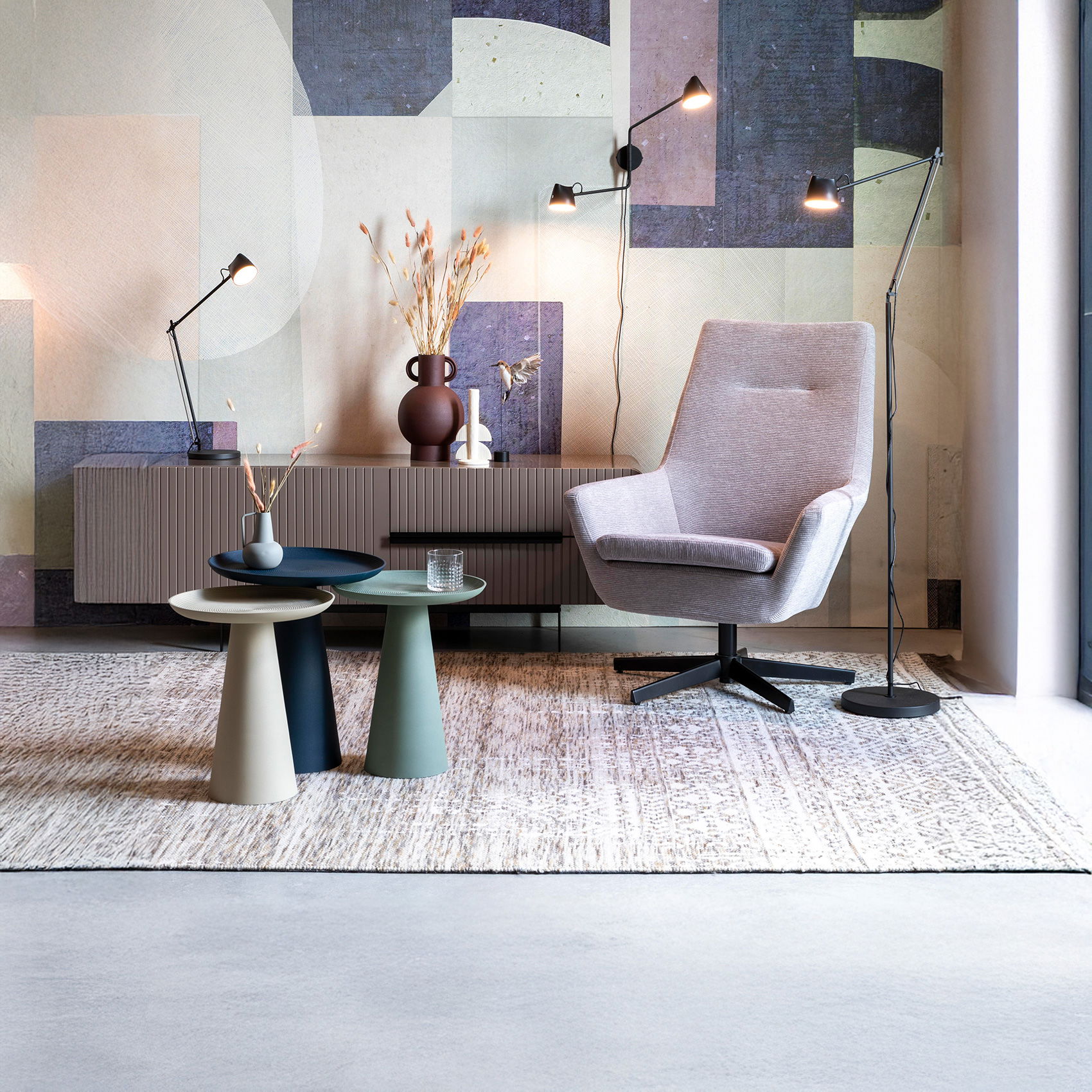 Modernes Wohnzimmer mit grauem Sessel, Beistelltischen, Sideboard, Designlampen und Wanddeko