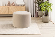 Beiger, runder Bouclé-Sitzpouf auf hellem Teppich in modernem Wohnzimmer, Frontansicht auf Augenhöhe