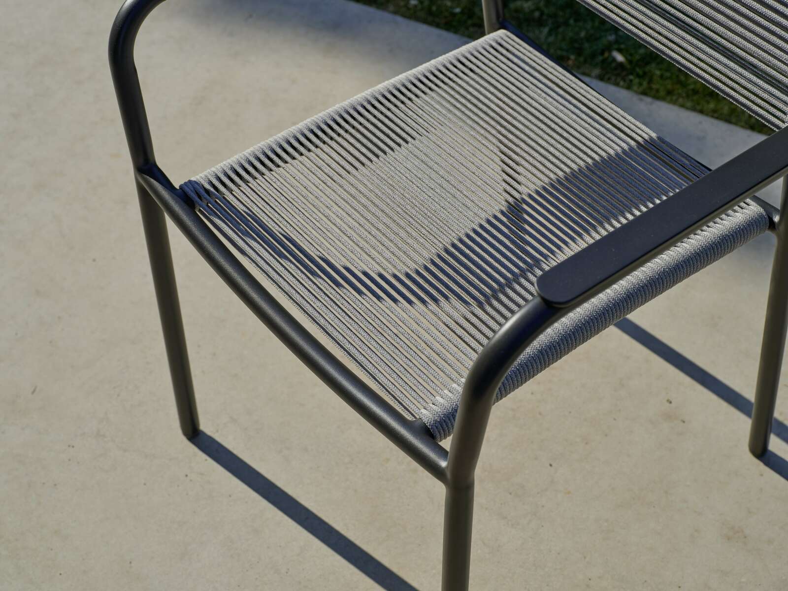 Nahaufnahme eines Stapelsessels mit Metallrahmen und geflochtener Sitzfläche, von oben betrachtet.