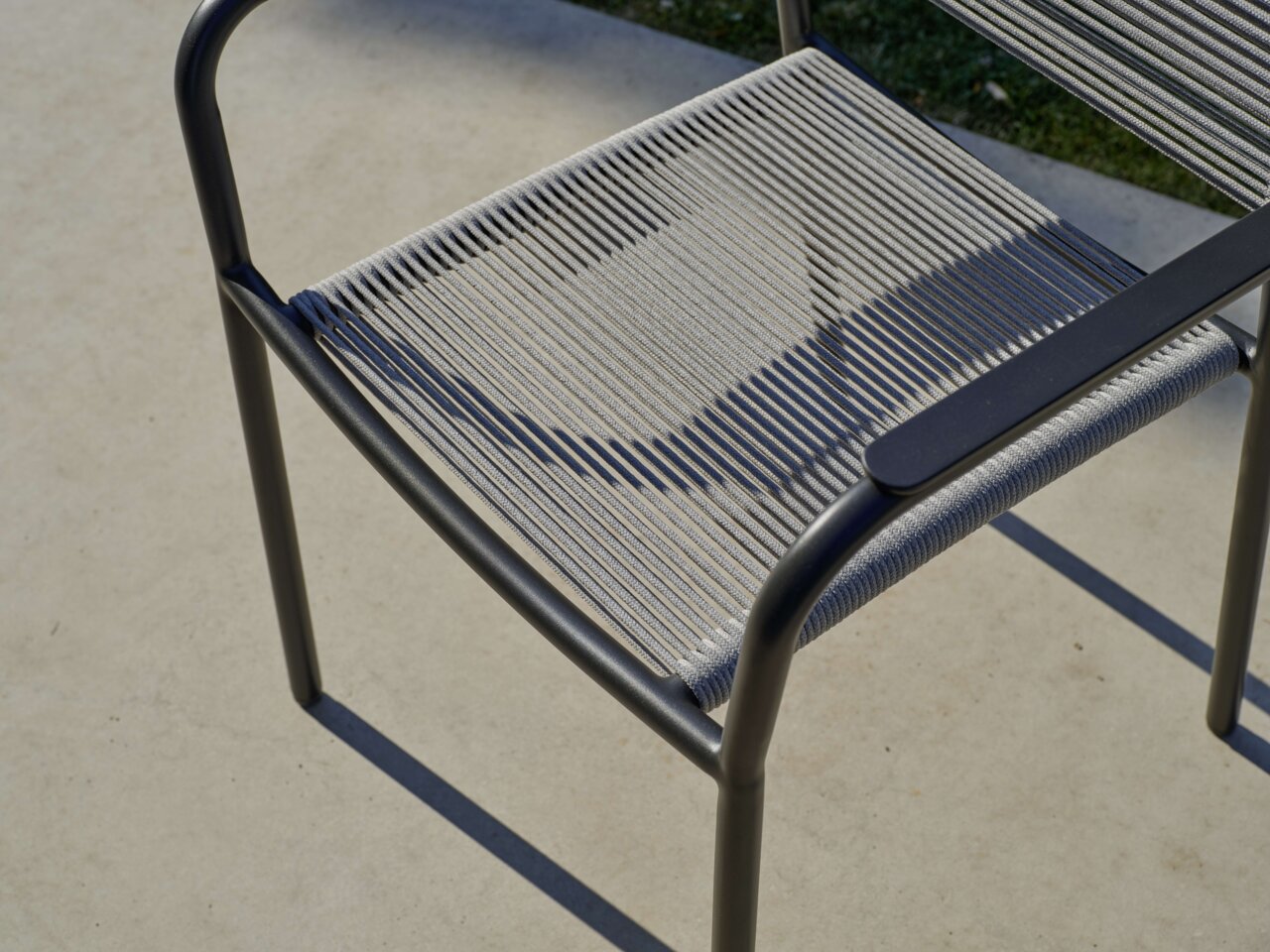 Close-up van een stapelstoel met metalen frame en gevlochten zitting, gezien van bovenaf.