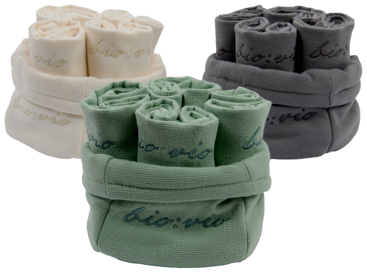 Drei Sets von Gästetüchern in den Farben Creme, Grün und Grau, aufgerollt und in passenden Stoffkörben präsentiert. Perspektive von vorne.