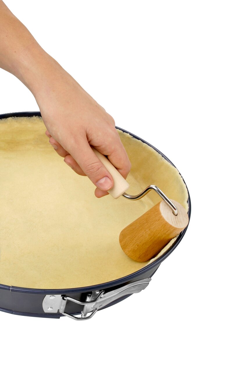 Dr. Oetker Houten deegroller Een hand houdt een kleine houten deegroller vast en rolt het deeg uit in een ronde bakvorm, gezien van bovenaf.