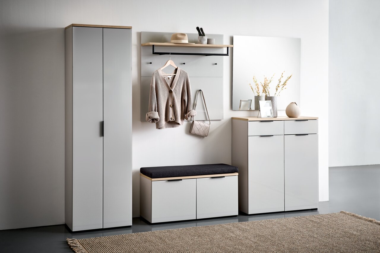 Voleo Schuhbank NEW YORK Moderne Garderobenkombination in hellem Raum, bestehend aus einem hohen Schrank, einem Garderobenpaneel mit Haken und Ablage, einer Schuhbank mit Sitzkissen und einem Schuhschrank mit Spiegel. Frontalansicht.