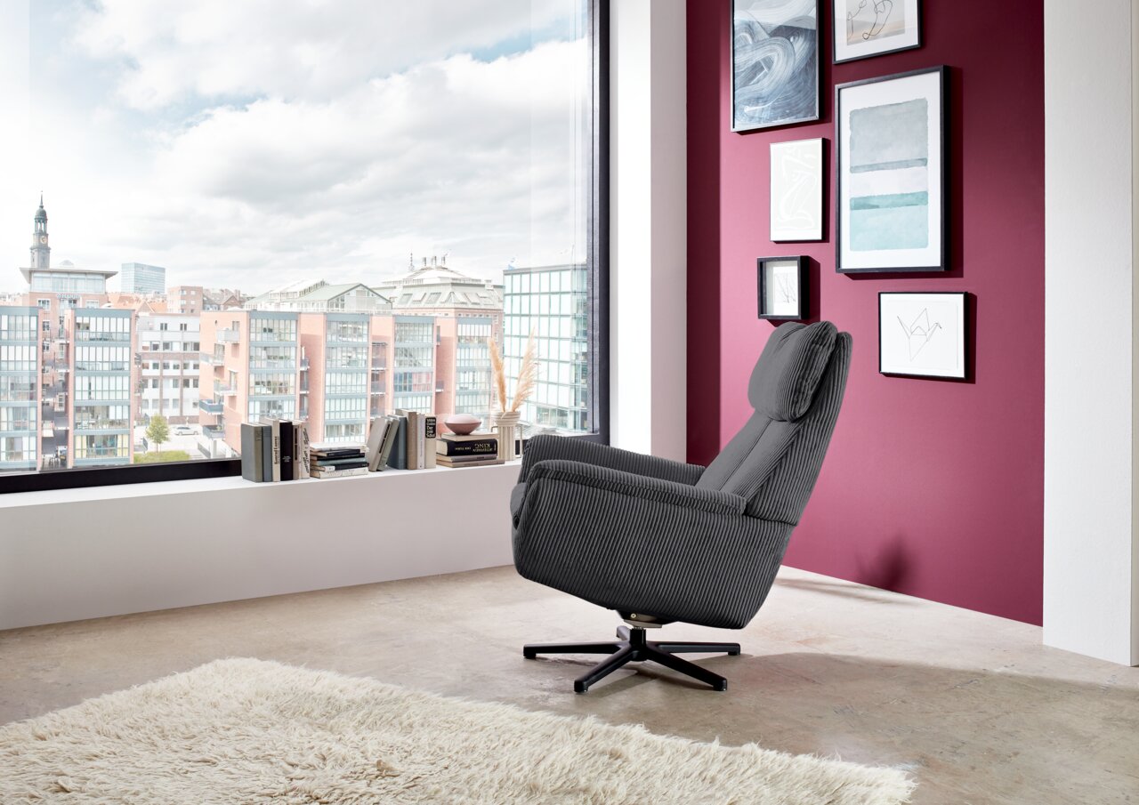 Beldomo Style Sessel LAGOS Grauer Sessel in einem modernen Raum mit Blick auf die Stadt, seitliche Perspektive.