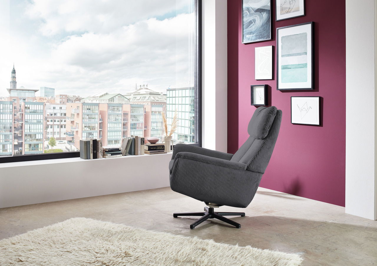 Beldomo Style Sessel LAGOS Grauer Sessel in einem modernen Raum mit Blick auf die Stadt, seitliche Perspektive.