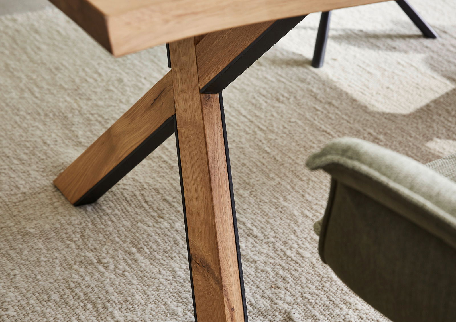 Nahaufnahme eines Esstischbeins aus Holz mit schwarzem Metallrahmen, auf einem hellen Teppich. Perspektive von der Seite.