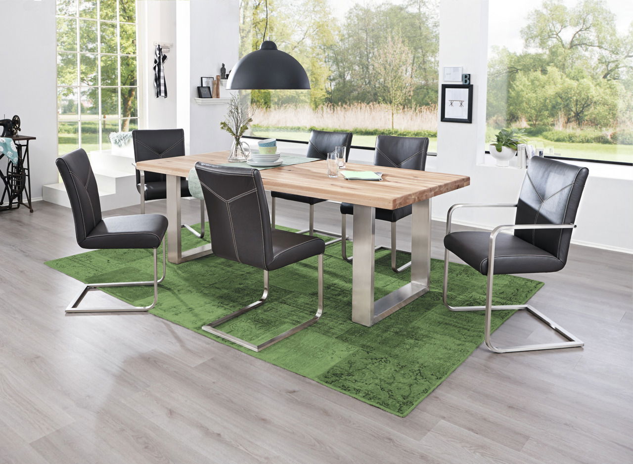 Moderner Essbereich mit einem großen Holztisch und sechs Freischwinger-Stühlen in einem hellen Raum mit großen Fenstern, Blick von der Seite.