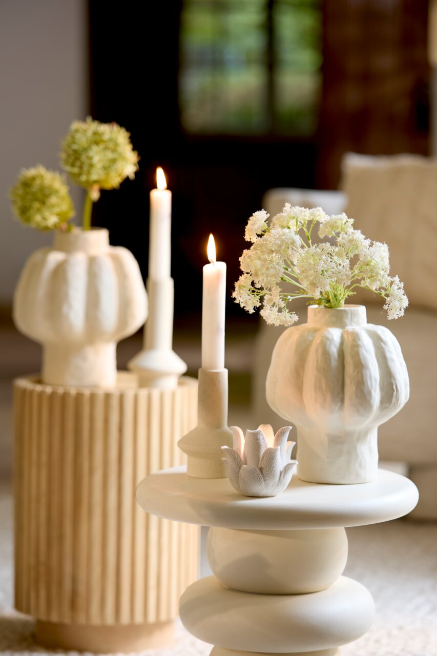 Ein stilvoller Kerzenständer in einem modernen, minimalistischen Design, umgeben von dekorativen Vasen mit Blumen, aus einer seitlichen Perspektive fotografiert.