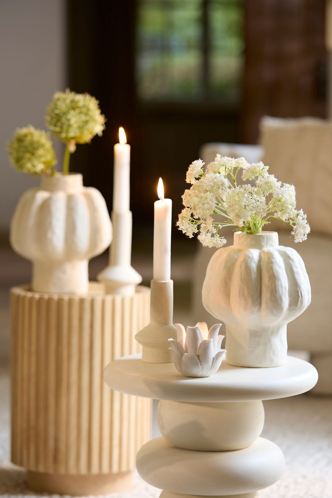 Ein stilvoller Kerzenständer in einem modernen, minimalistischen Design, umgeben von dekorativen Vasen mit Blumen, aus einer seitlichen Perspektive fotografiert.