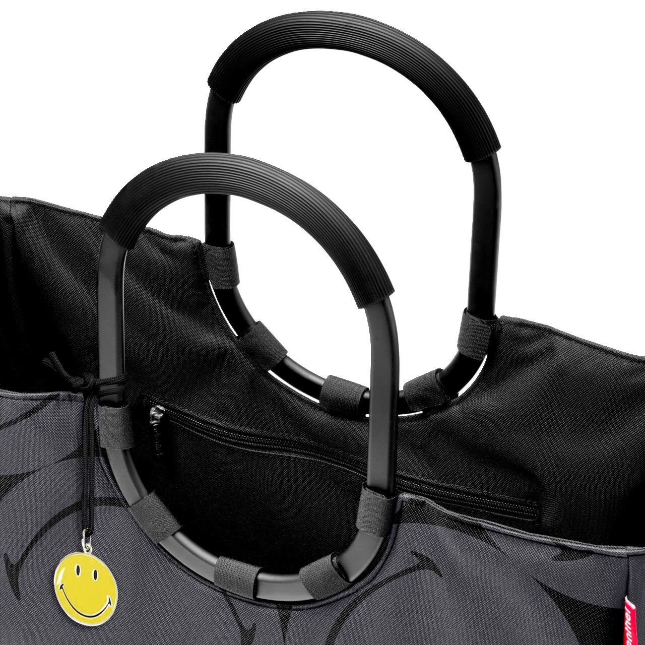 Nahaufnahme einer schwarzen Tasche mit großen, runden Griffen und einem gelben Smiley-Anhänger, von oben betrachtet.