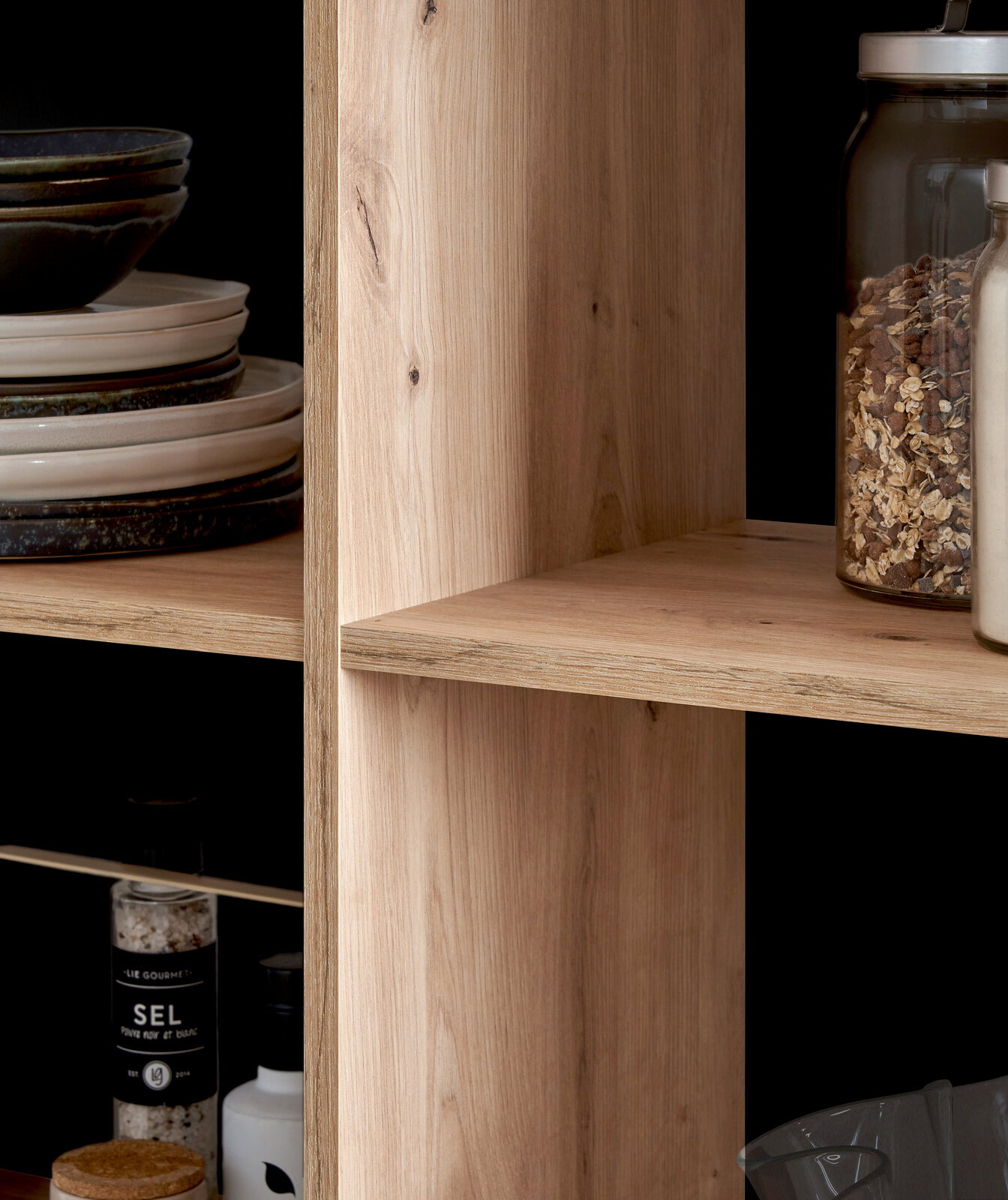 Nahaufnahme eines Holzregals mit Geschirr und Vorratsgläsern, seitliche Perspektive.