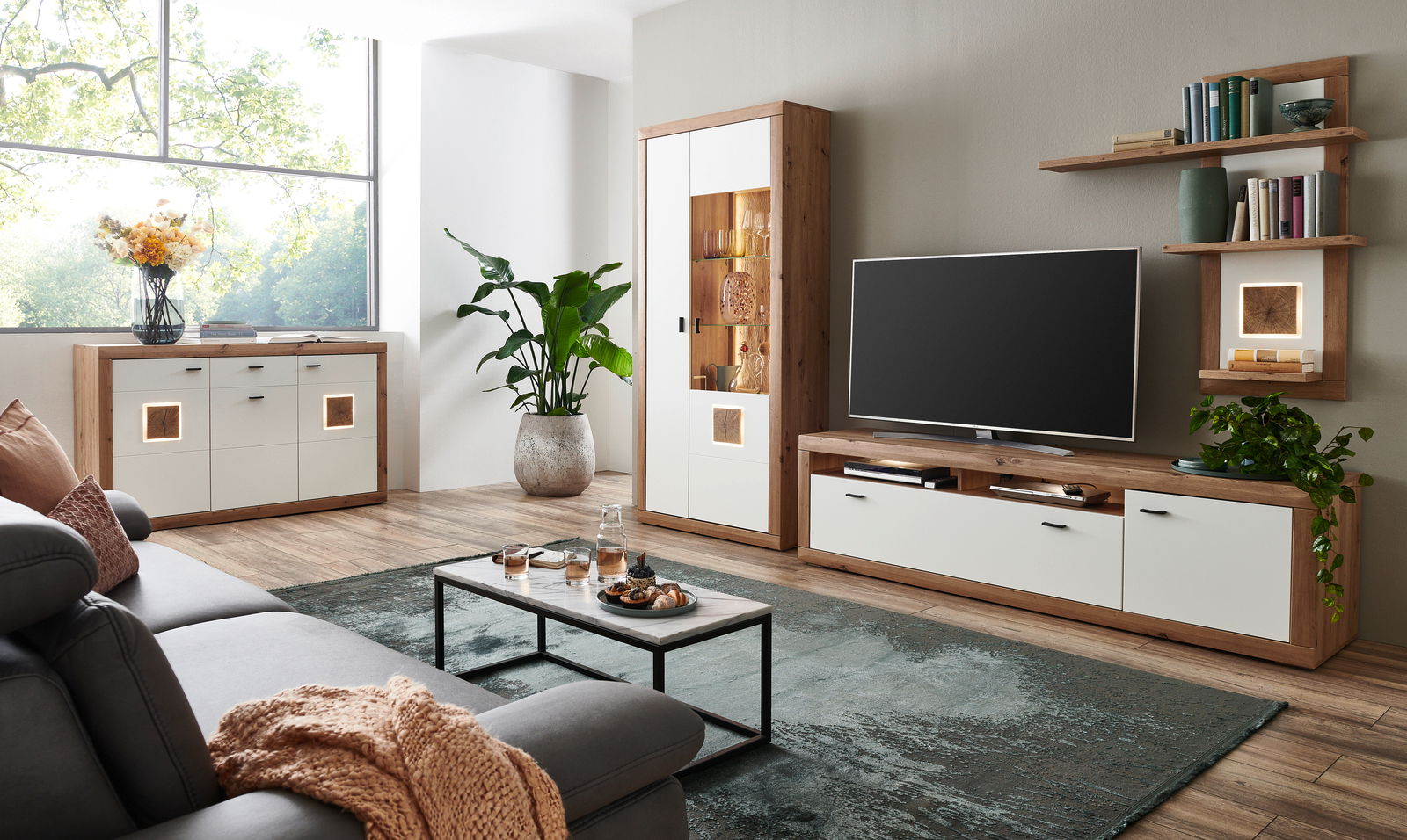 Moderne Wohnzimmerkombination mit Holz- und Weißakzenten, bestehend aus Sideboard, Vitrine und TV-Board, seitliche Perspektive.