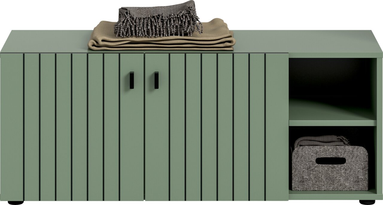 Grünes Sideboard mit Lamellenfront und zwei Griffen, rechts offene Regalfächer mit Stoffbox und gefalteten Textilien, oben Decke und Fransenschal; Frontalansicht.