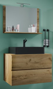 Frontale Ansicht eines modernen Badezimmer-Waschtischs in Holzoptik mit schwarzem Aufsatzwaschbecken und Armatur, darüber Spiegel mit Holzrahmen, Ablage und LED-Spiegelleuchte an grüner Wand