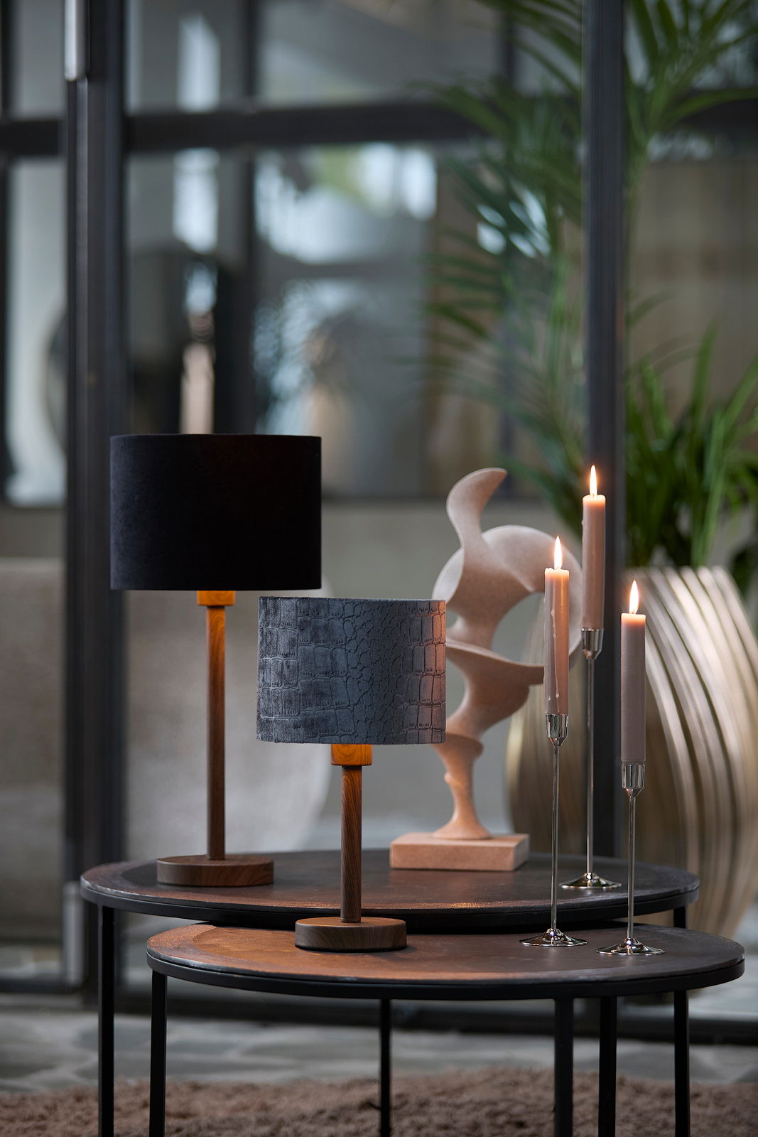 Elegante Kerzenständer mit brennenden Kerzen auf einem Tisch, im Hintergrund moderne Lampen und Dekorationen. Perspektive von vorne.