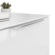 Nahaufnahme einer weißen Nachtkommode mit glänzender Oberfläche, silbernem Griff und Dekorationen wie einem kleinen Pflanzentopf und Büchern auf der Oberseite, aus seitlicher Perspektive.