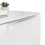 Nahaufnahme einer weißen Nachtkommode mit glänzender Oberfläche, silbernem Griff und Dekorationen wie einem kleinen Pflanzentopf und Büchern auf der Oberseite, aus seitlicher Perspektive.