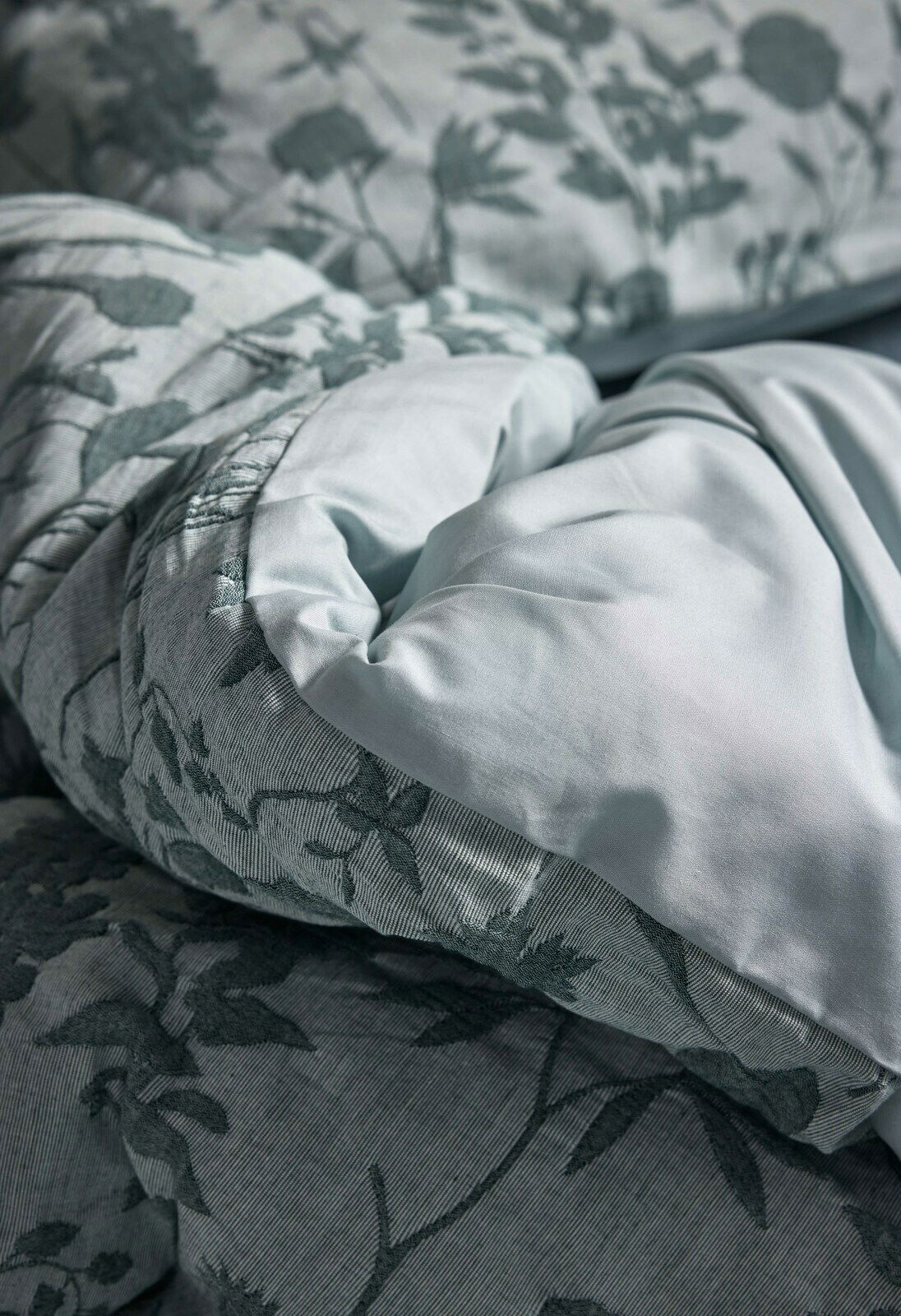 Nahaufnahme von Bettwäsche mit floralem Muster in sanften Grüntönen, Perspektive von oben