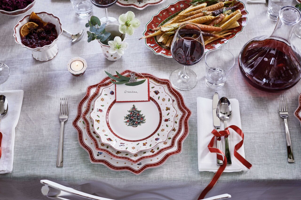 Weihnachtlich gedeckter Tisch mit einem Frühstücksteller in Weiß mit rotem Rand und Weihnachtsbaum-Motiv, von oben fotografiert.