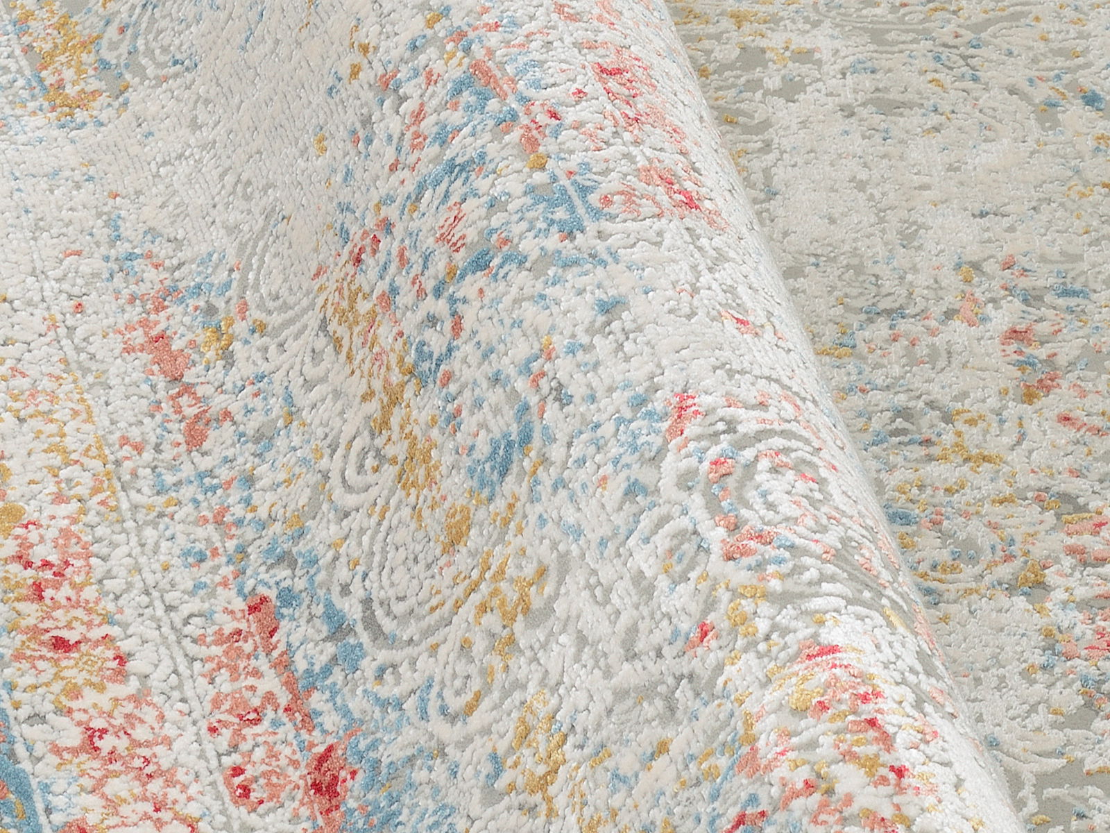 Nahaufnahme eines Designer-Teppichs mit buntem Muster in Rot, Blau und Gelb auf weißem Hintergrund, perspektivisch von der Seite aufgenommen.