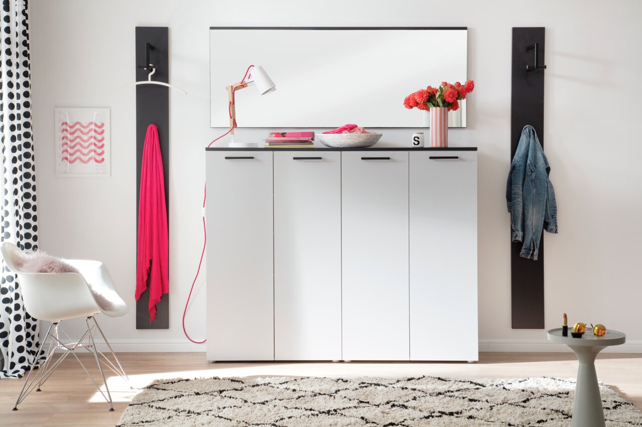 Moderano Spiegel ALMADA Moderner Flur mit weißem Schrank, darüber ein rechteckiger Spiegel, seitlich Garderobenhaken mit Kleidung, aus der Frontalperspektive.