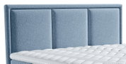 Vooraanzicht van een bed met een hoog, lichtblauw gestoffeerd hoofdbord met drie verticale panelen en een witte, doorgestikte matras.
