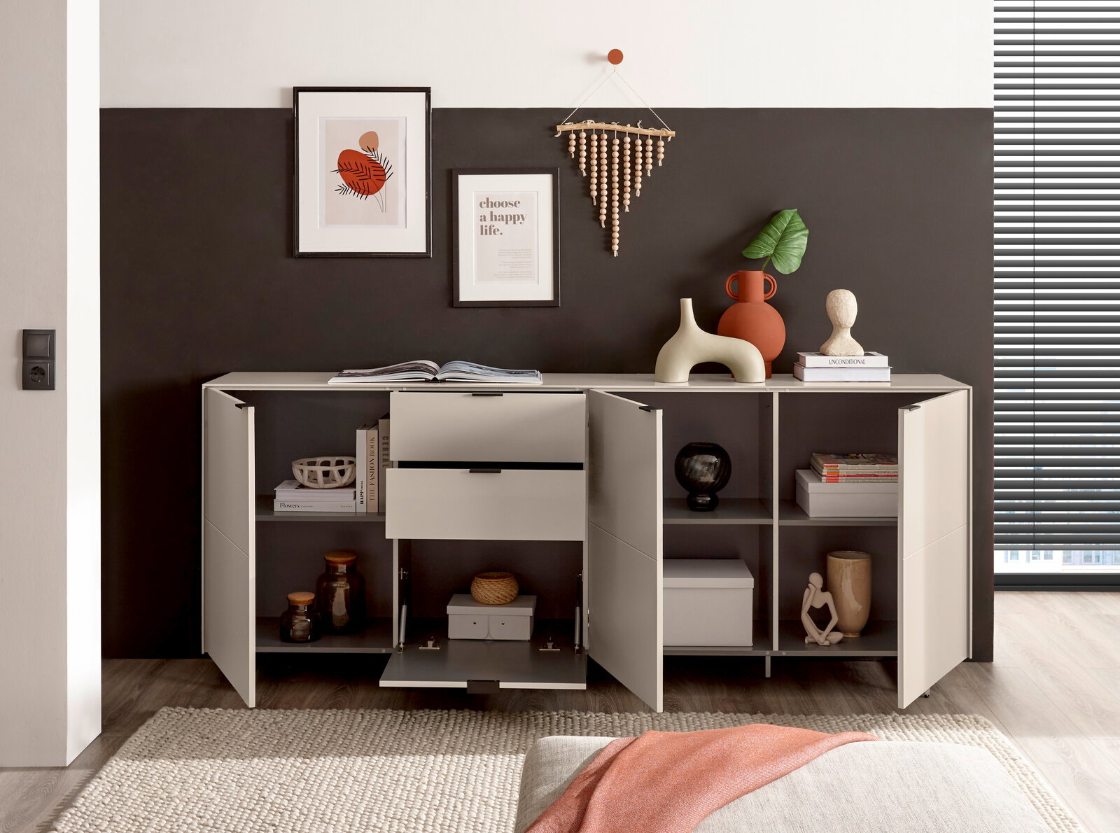 Modernes weißes Sideboard mit offenen Türen und Schubladen, dekoriert mit Vasen, Büchern und Wandbildern; frontale Perspektive im Wohnraum.