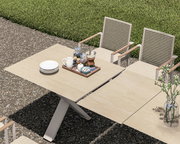 Garten Ausziehtisch aus hellem Holz mit modernen Stühlen, von oben fotografiert, auf einer Terrasse mit grüner Wiese im Hintergrund.