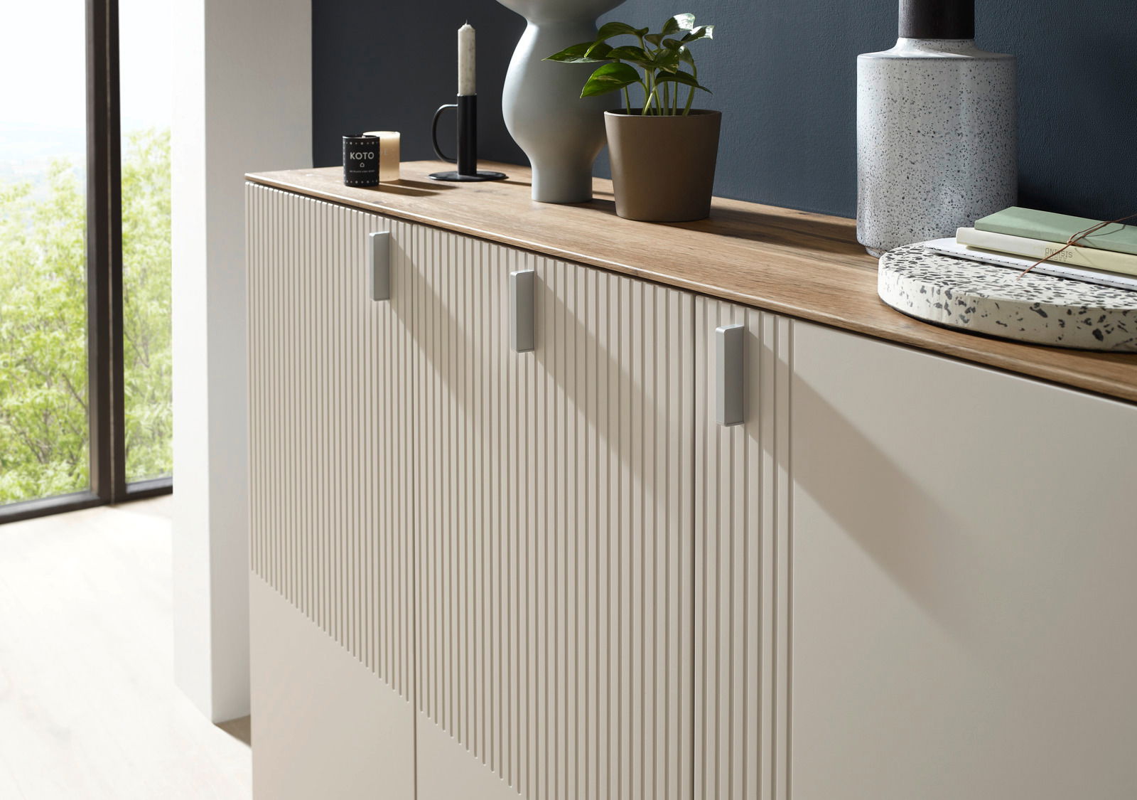 Seitliche Perspektive auf einen XL-Schuhschrank mit gerillten Türen, einer Holzoberfläche und dekorativen Elementen wie Pflanzen und Kerzen.