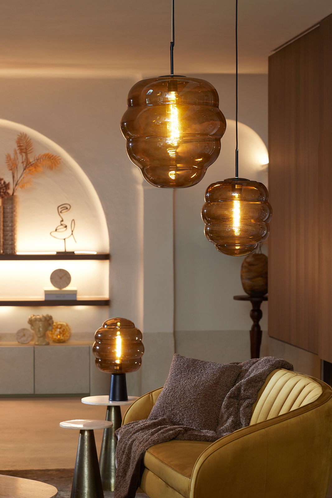 Gemütliches Wohnzimmer mit braunem Kissen auf einem gelben Sofa, umgeben von stilvollen, hängenden und stehenden Lampen in warmem Licht.