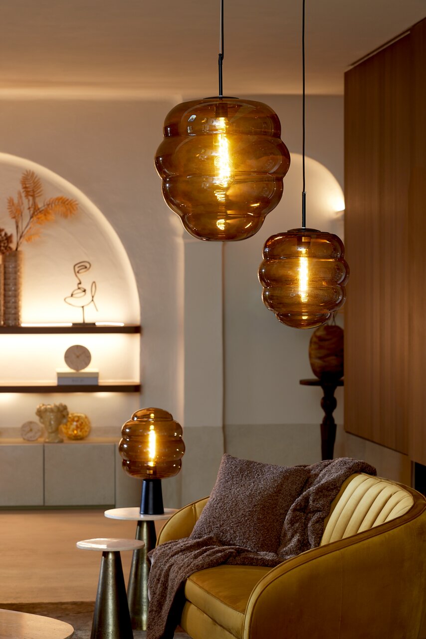 Gemütliches Wohnzimmer mit braunem Kissen auf einem gelben Sofa, umgeben von stilvollen, hängenden und stehenden Lampen in warmem Licht.