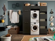 Moderner Waschraum mit einem schwarzen Hochschrank, der eine Waschmaschine und einen Trockner enthält. Perspektive von vorne.