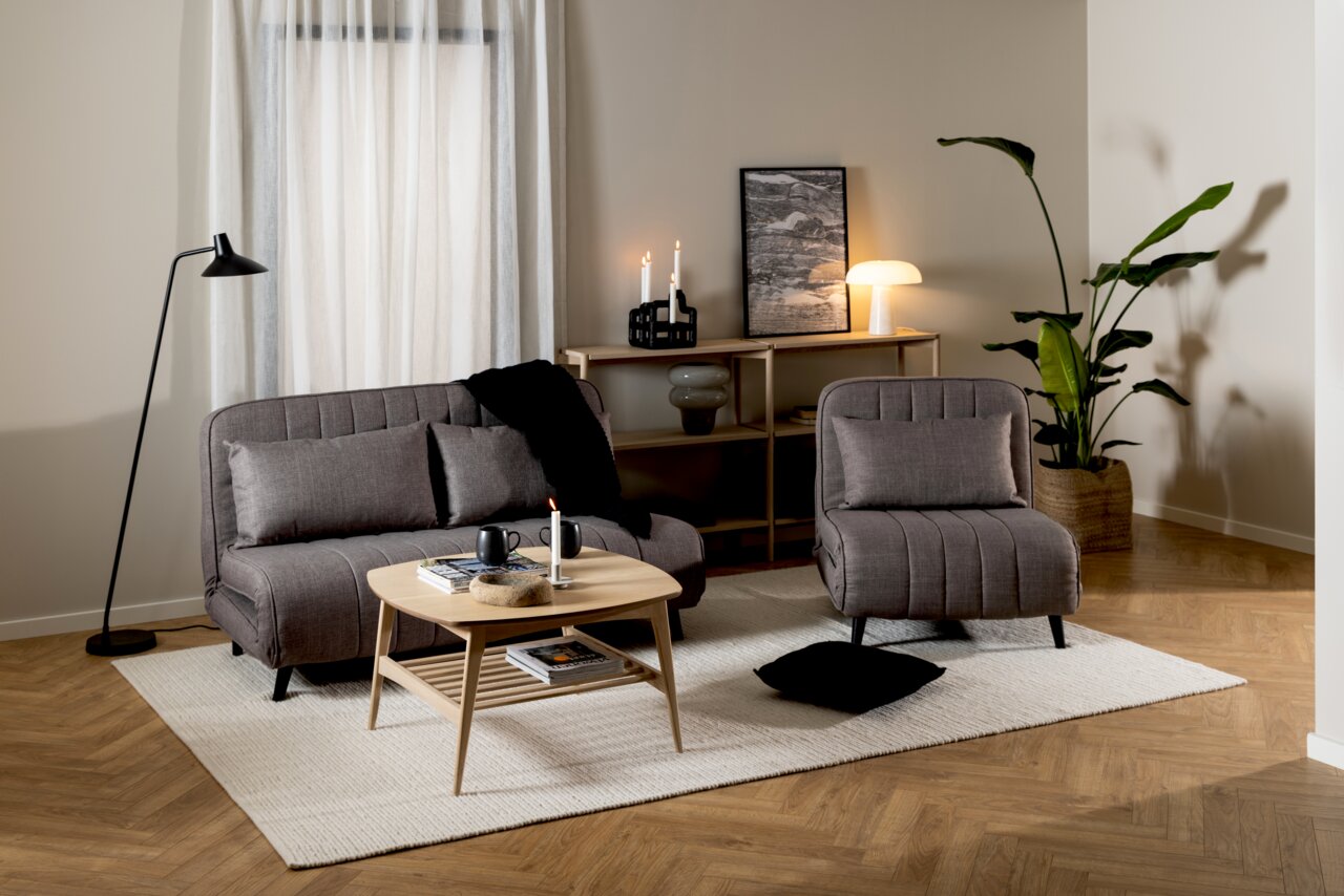 Modernes Wohnzimmer mit einem Regal im Hintergrund, dekoriert mit Kerzen und einer Lampe, aus der Perspektive von vorne betrachtet.