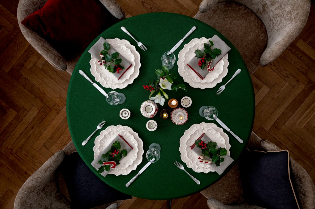 Vogelperspektive auf einen festlich gedeckten Tisch mit grünem Tischtuch, weißen Tellern, Besteck und weihnachtlicher Dekoration.