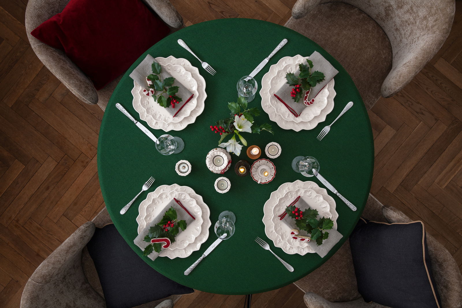 Vogelperspektive auf einen festlich gedeckten Tisch mit grünem Tischtuch, weißen Tellern, Besteck und weihnachtlicher Dekoration.
