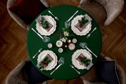 Vogelperspektive auf einen festlich gedeckten Tisch mit grünem Tischtuch, weißen Tellern, Besteck und weihnachtlicher Dekoration.