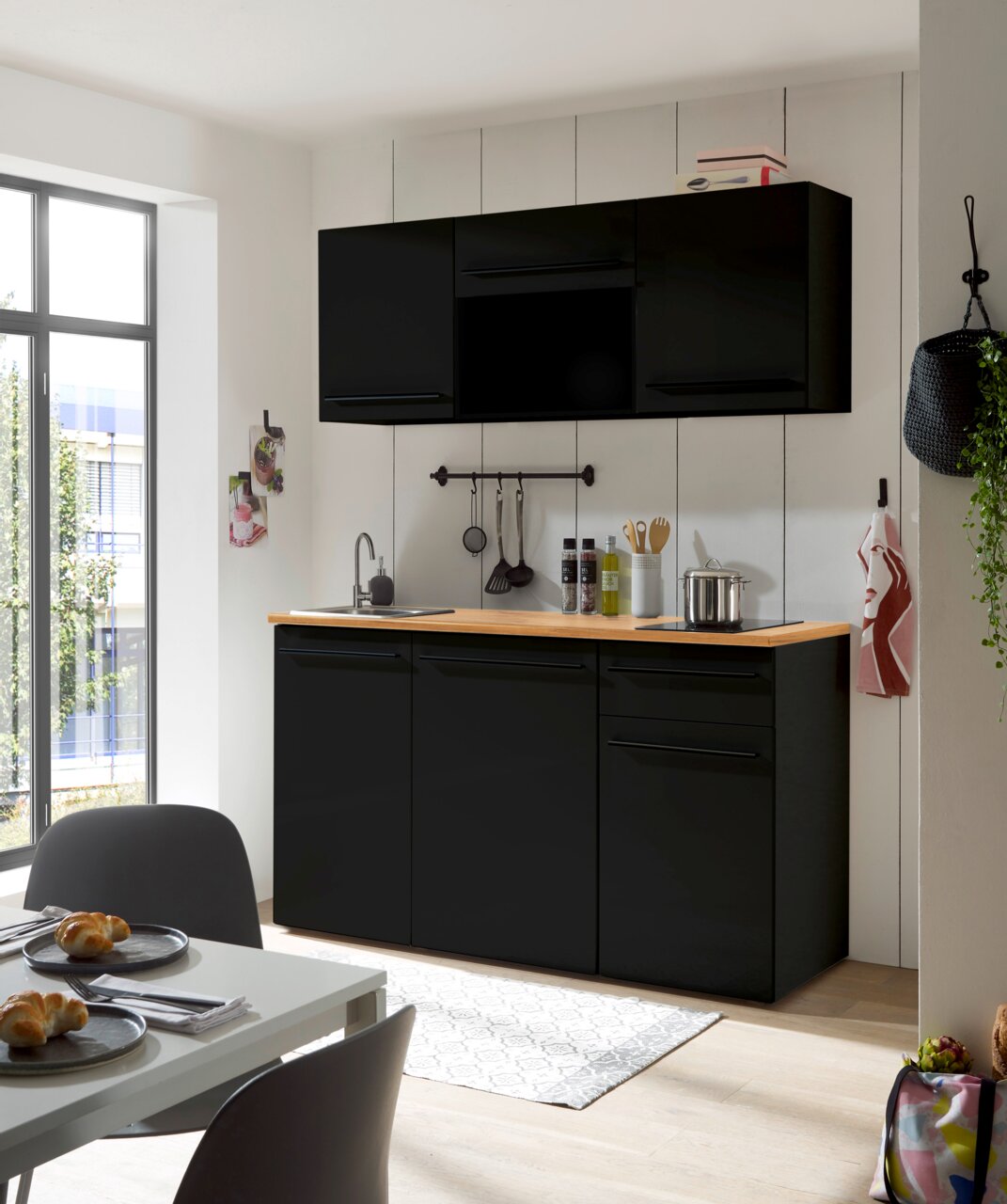 Moderne Single-Küche in schwarzem Design mit Holzarbeitsplatte, fotografiert aus einer leicht seitlichen Perspektive.