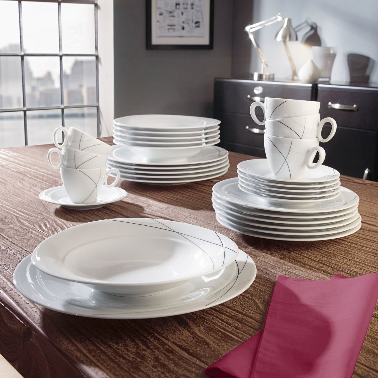 Elegant wit koffieservies met een modern lijnpatroon, bestaande uit kopjes, schoteltjes en borden, opgesteld op een houten tafel in een stijlvolle ruimte, gezien vanuit een zijdelingse hoek.