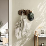 Wandgarderobe aus Holz mit mehreren Haken, an der eine Tasche und eine Mütze hängen, seitliche Perspektive.