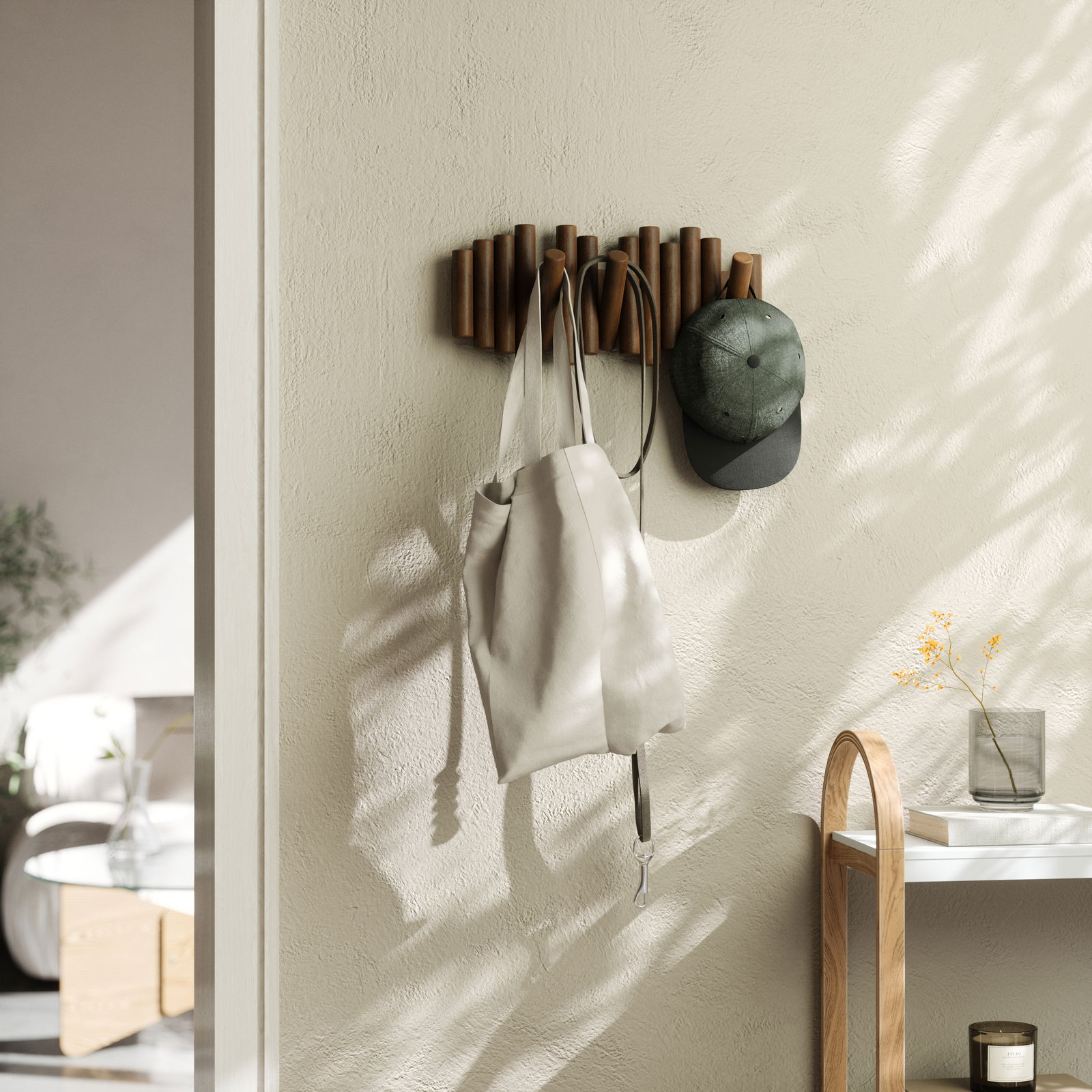 Wandgarderobe aus Holz mit mehreren Haken, an der eine Tasche und eine Mütze hängen, seitliche Perspektive.