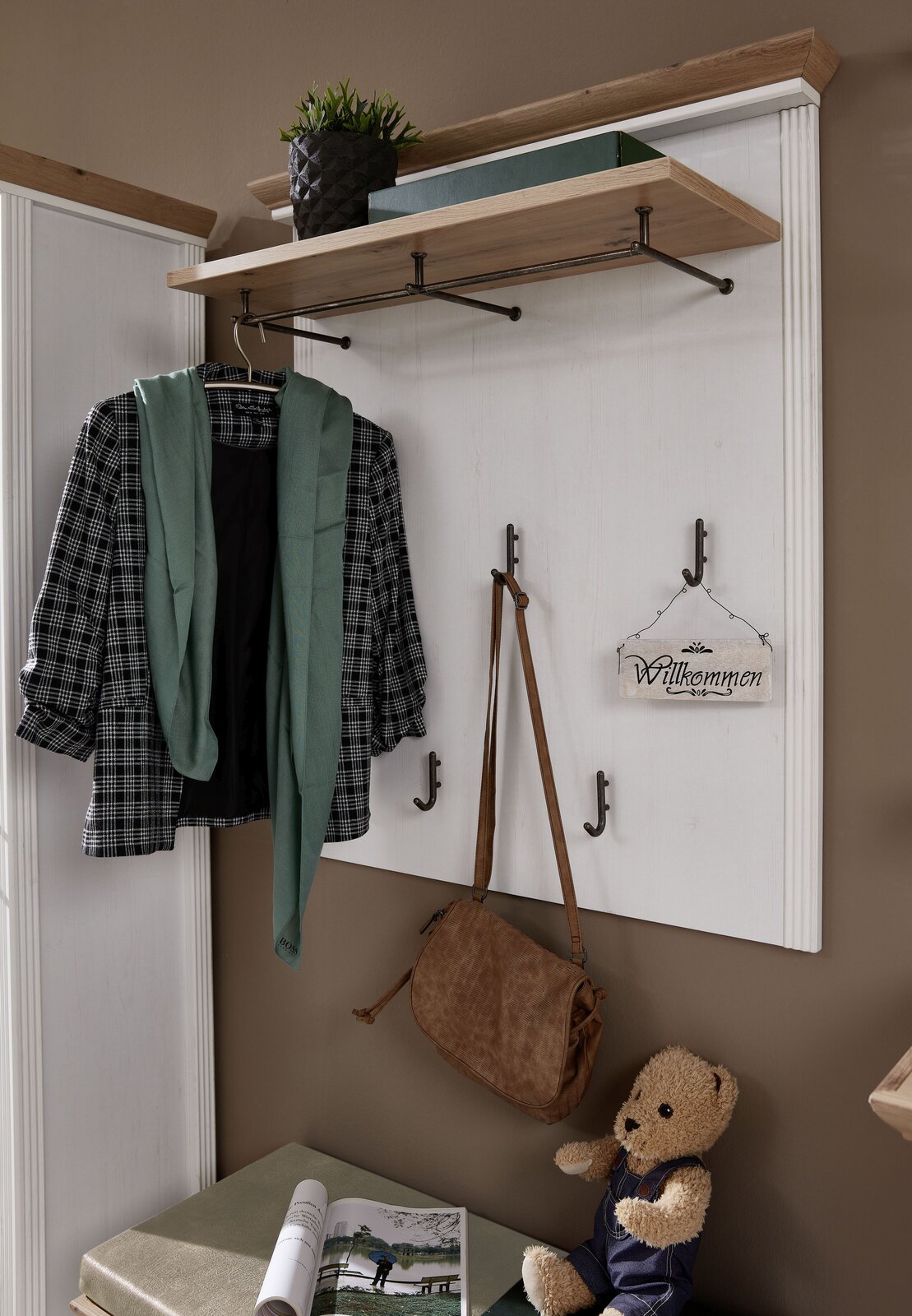 Garderobenpaneel mit Haken und Ablage, frontal fotografiert. Dekoriert mit Jacke, Schal, Tasche und Willkommensschild.