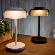 Zwei LED Tischleuchten in modernem Design, eine in Weiß und eine in Schwarz, auf einem Tisch stehend, seitliche Perspektive.