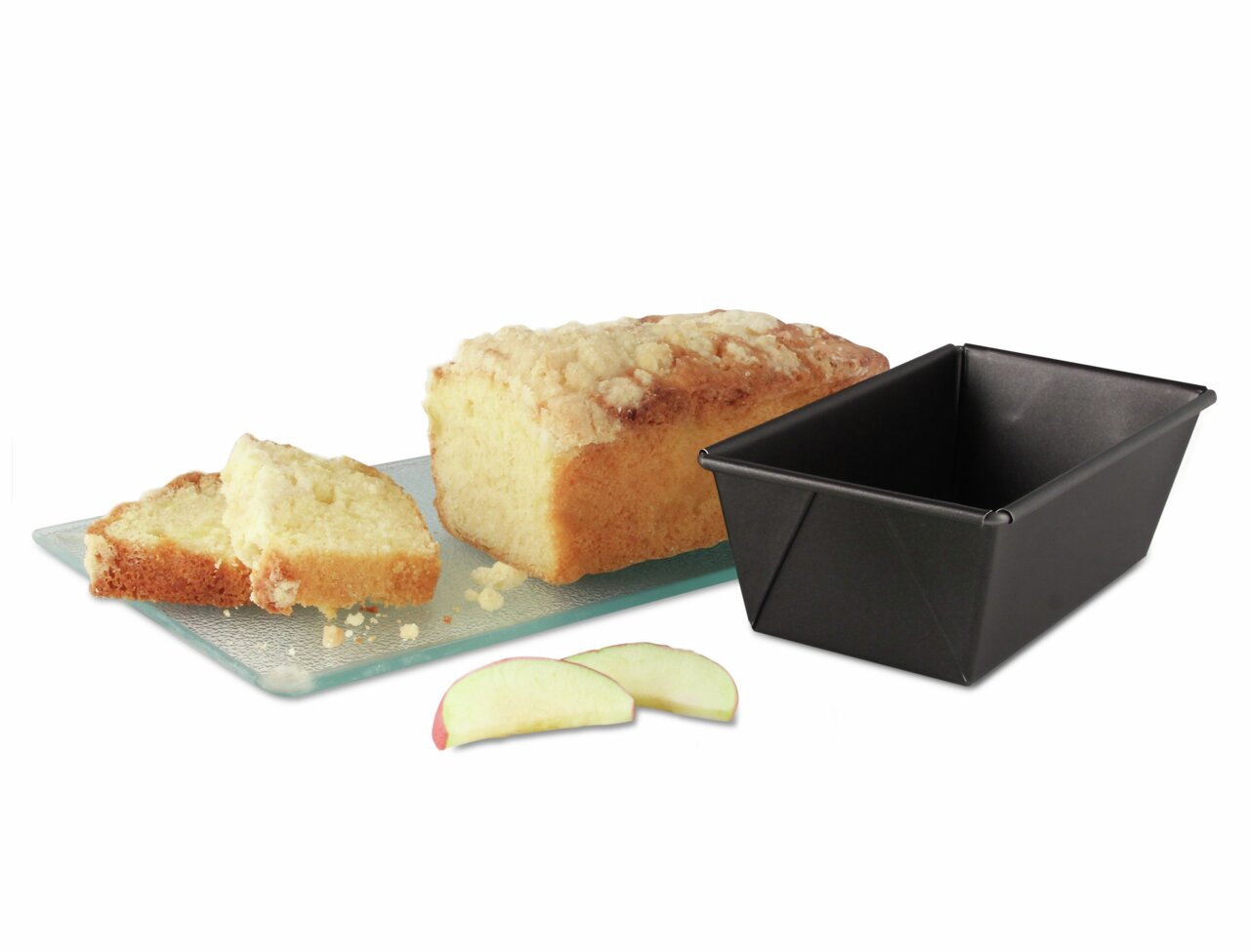 Kastenform 15cm BackFreude Min aus schwarzem Material, neben einem frisch gebackenen Kuchen auf einem Glasbrett, mit Apfelscheiben im Vordergrund. Perspektive von schräg oben.