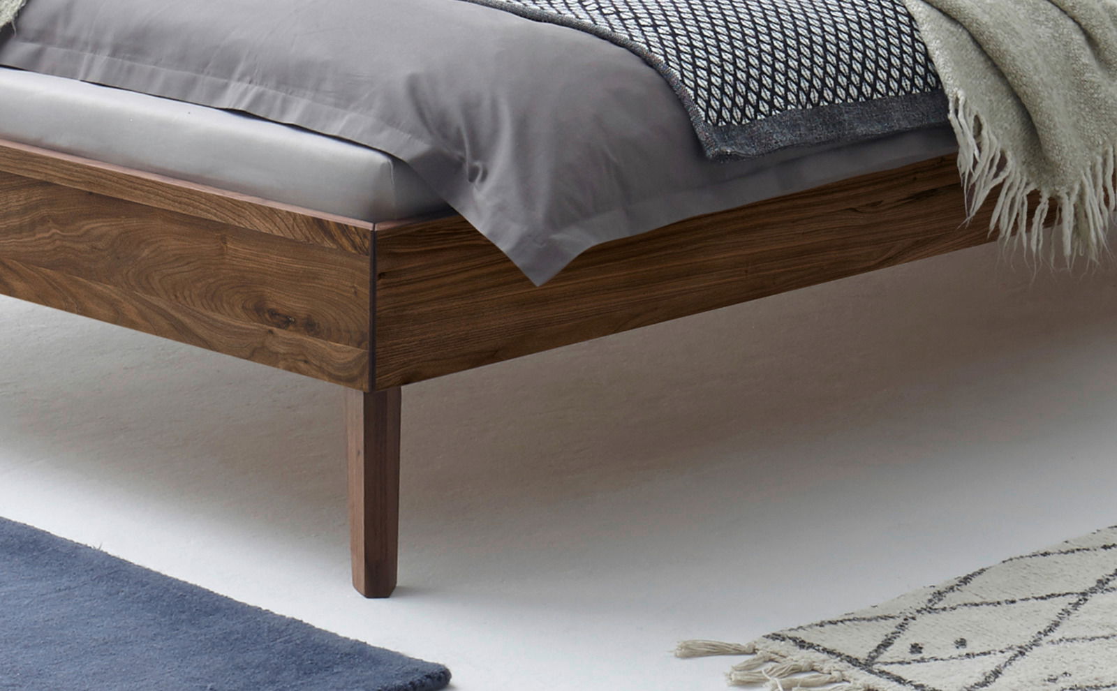 Nahaufnahme eines Bettgestells aus Holz mit Bettwäsche in einer seitlichen Perspektive.