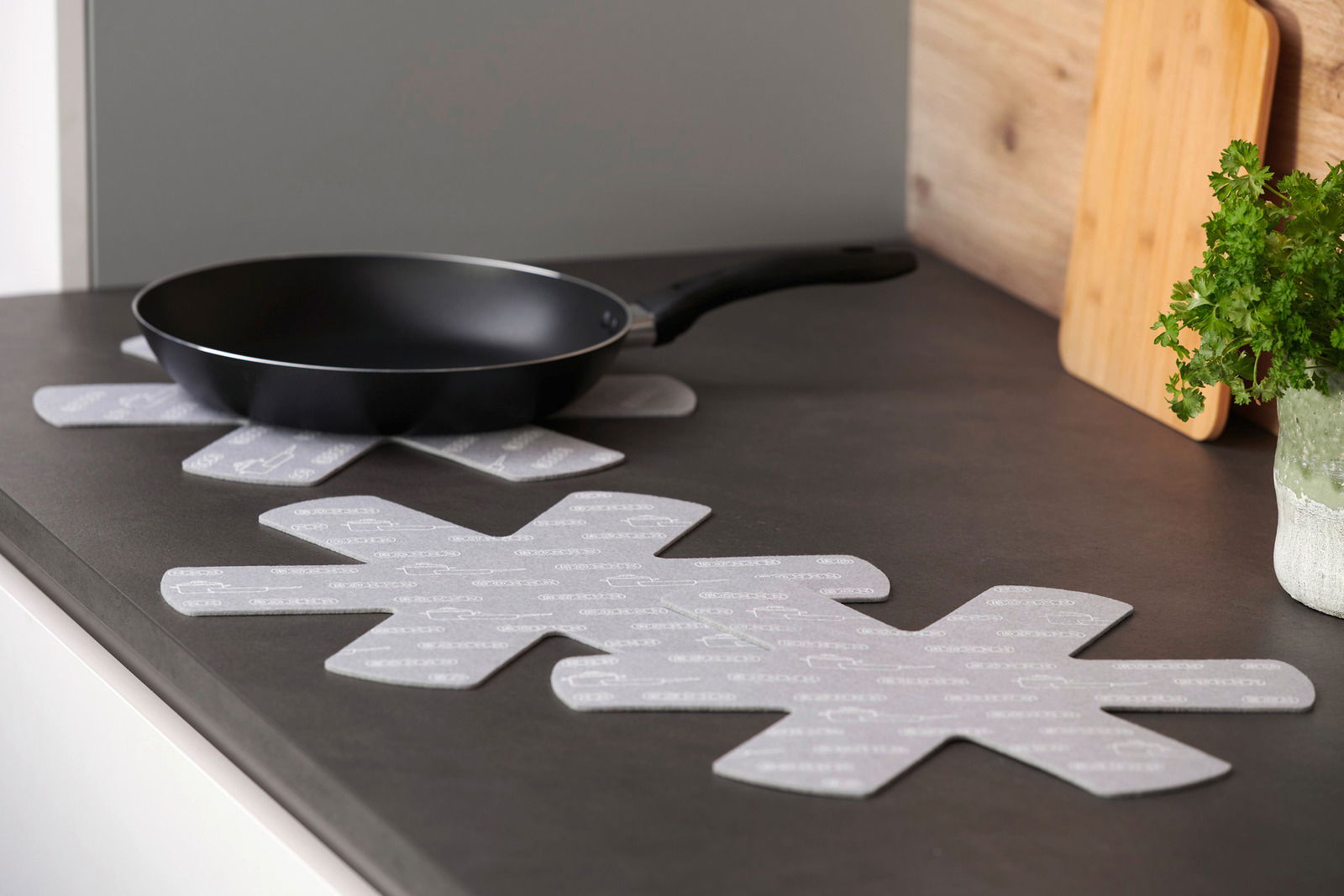 Pfannenschutz in Sternform auf einer Küchenarbeitsplatte, mit einer Pfanne darauf platziert, seitliche Perspektive.