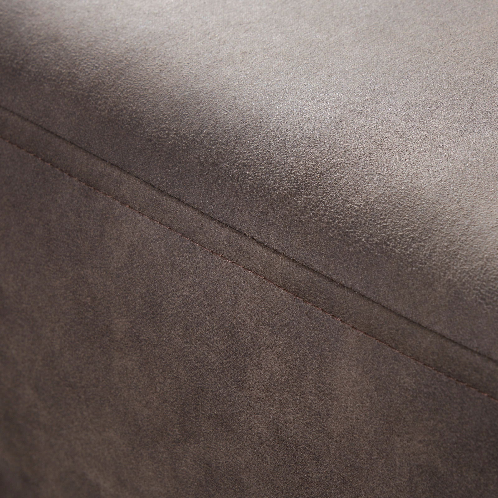 Nahaufnahme einer braunen, texturierten Oberfläche eines Möbelstücks, möglicherweise ein Hocker oder eine Rundecke, mit sichtbarer Naht. Perspektive von oben.