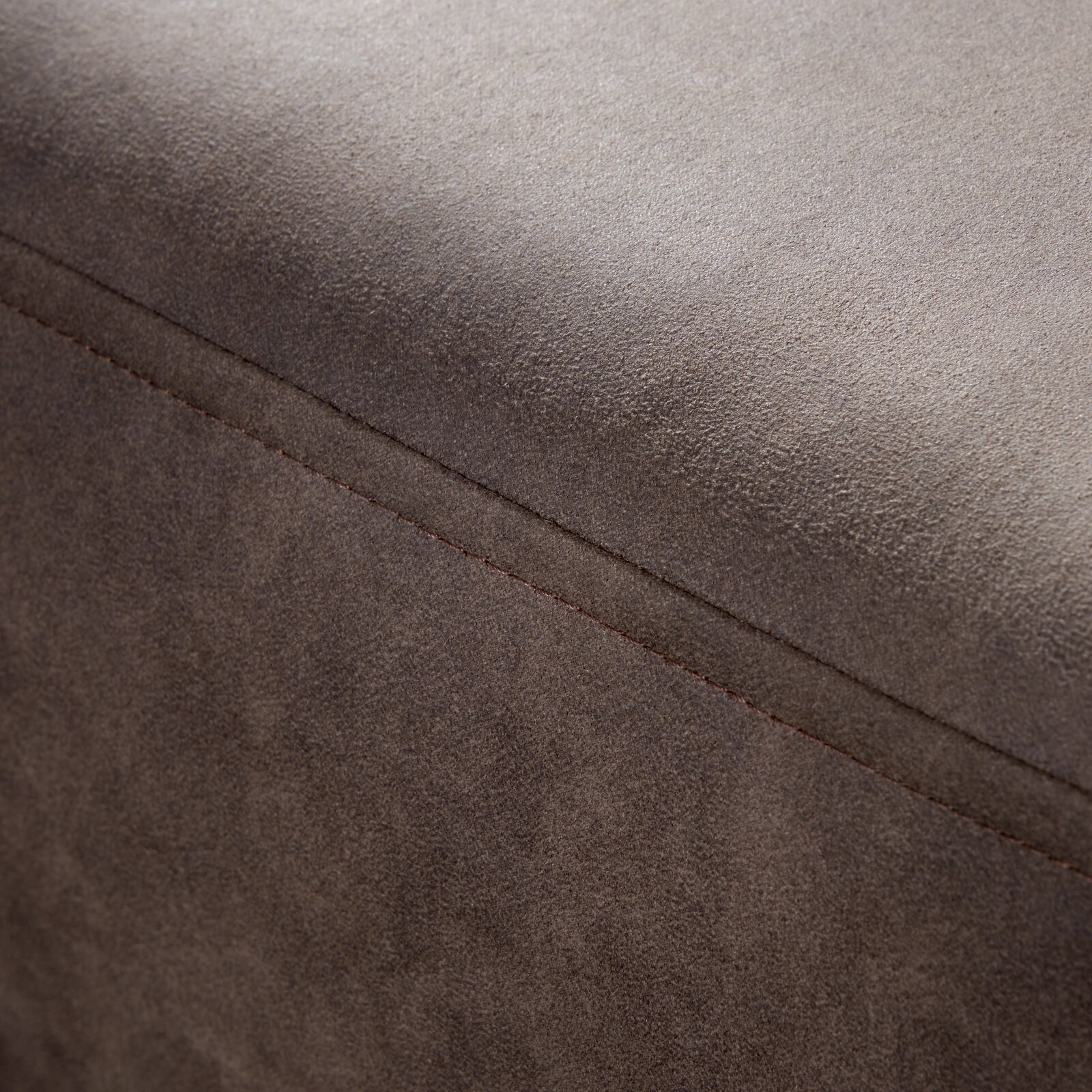 Nahaufnahme einer braunen, texturierten Oberfläche eines Möbelstücks, möglicherweise ein Hocker oder eine Rundecke, mit sichtbarer Naht. Perspektive von oben.