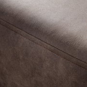 Nahaufnahme einer braunen, texturierten Oberfläche eines Möbelstücks, möglicherweise ein Hocker oder eine Rundecke, mit sichtbarer Naht. Perspektive von oben.