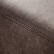 Nahaufnahme einer braunen, texturierten Oberfläche eines Möbelstücks, möglicherweise ein Hocker oder eine Rundecke, mit sichtbarer Naht. Perspektive von oben.